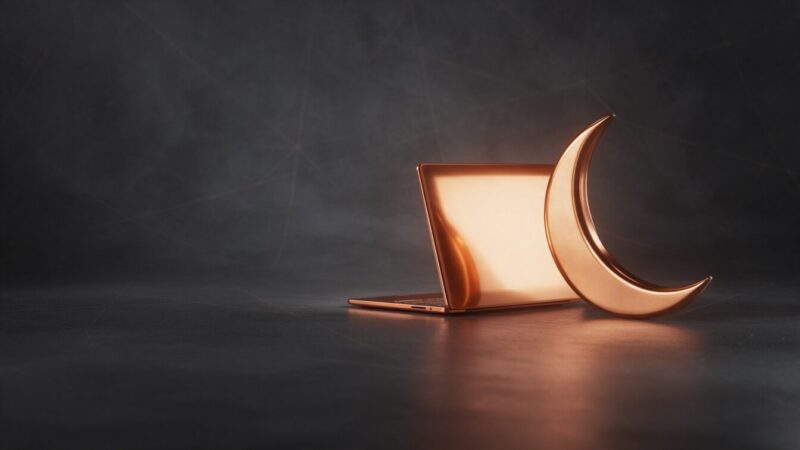 Notebook de cobre com a tela iluminada em âmbar ao lado de uma lua crescente de cobre, representando o site que atende o cliente fora do horário comercial