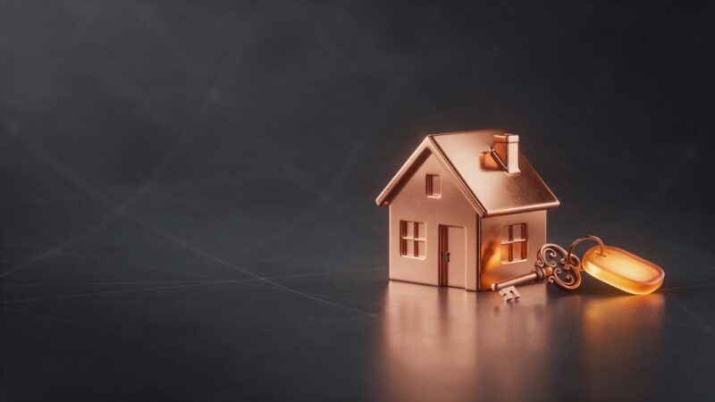 Casa de cobre em miniatura ao lado de uma chave de cobre, representando o site da imobiliária que atende proprietário e comprador